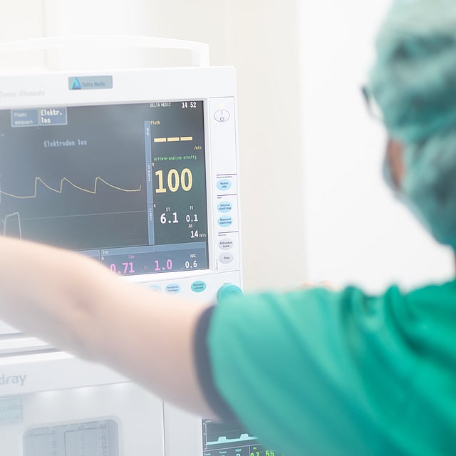 Een persoon in scrubs en chirurgische kap die aan een medische monitor werkt.