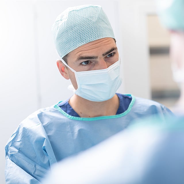 Een persoon die chirurgische scrubs en masker draagt.