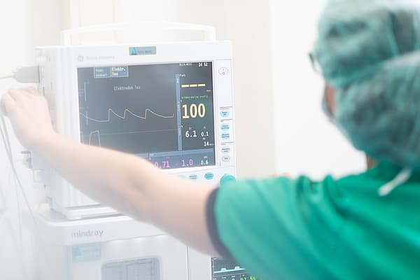 Een persoon in scrubs en chirurgische kap die aan een medische monitor werkt.